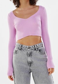 Pink ribbed cropped sweater with long sleeves, V-neckline, paired with high-waisted gray denim jeans featuring a faded texture.