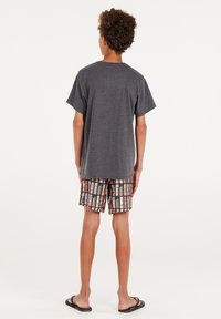 Grijze katoenen t-shirt met korte mouwen, gecombineerd met multikleurige shorts met een patroon van winkelramen op een zwarte achtergrond.