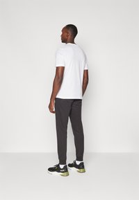 White short-sleeve t-shirt, black joggers, and black sneakers with green accents. Smooth fabric, relaxed fit, and elastic cuffs.