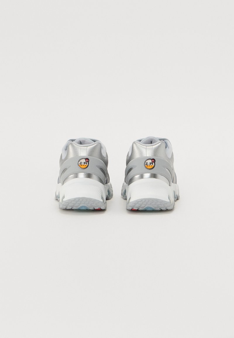 Zapatillas deportivas plateadas con una media suela texturizada, parte superior de malla y un logotipo distintivo en el talón. Cuenta con un diseño acolchado y suela de goma.