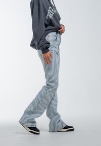 Vaqueros de mezclilla azul claro de corte acampanado con un sutil patrón de rayas de cebra, combinados con una sudadera gris y zapatillas negras con acentos blancos.