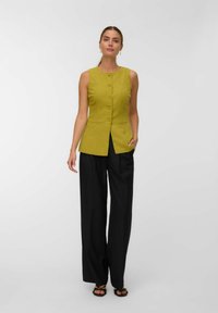 Gilet en lin de couleur jaune vif avec un design raffiné, présentant des boutons sur le devant et deux poches latérales. Assorti à un pantalon large noir.
