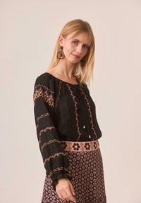 Blusa negra con bordados en rosa y mangas fruncidas, combinada con una falda estampada que presenta diseños florales y una cinturilla rosa.