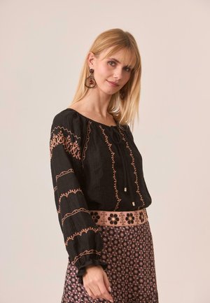 Blusa negra con bordados en rosa y mangas fruncidas, combinada con una falda estampada que presenta diseños florales y una cinturilla rosa.