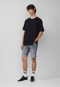 Czarna koszulka krótkiego rękawa z kieszonką, zestawiona z podwiniętymi szarymi dżinsowymi szortami. Uzupełniona czarnymi trampkami i białymi skarpetami w czarne paski.