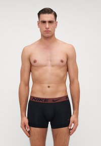 Czarne męskie bokserki z bordowym pasem, na którym widnieje napis "NIKE". Wykonane z gładkiego materiału, mają dopasowany krój oraz krótkie nogawki.