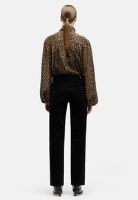 Blusa de estampado de leopardo con mangas largas, combinada con unos vaqueros negros de cintura alta. El conjunto incluye elegantes botas anchas negras.