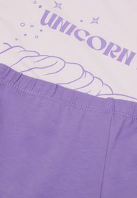 Lila Baumwolloberteil mit einem weißen Grafikdesign und dem Text "UNICORN", einem Hornmotiv und einem strukturierten Taillenbanddetail.
