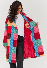 Farebný patchworkový plášť do dažďa s rôznymi potlačami zvierat, s gombíkovým zapínaním a hladkou červenou podšívkou s vnútornou kapsou.