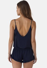 Mono de satén azul marino con tirantes finos, espalda en forma de V profunda y pantalones cortos con volantes. Textura suave y cinturilla elástica para mayor comodidad.