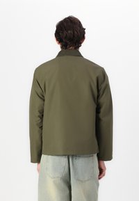 Olive green, lightweight jacket with a collar, long sleeves, and a straight cut. Material appears smooth, featured with minimal hardware.