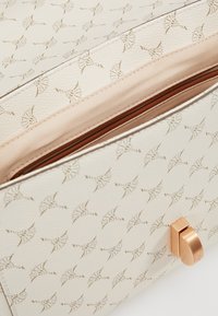 Borsa a mano crema con motivo impresso, hardware color oro rosa e una texture liscia. Presenta un'apertura con zip e una fodera in tessuto a contrasto.
