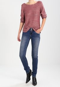 Pull en maille rouge avec un col large et des manches trois-quarts, associé à un jean skinny bleu et des bottines noires.