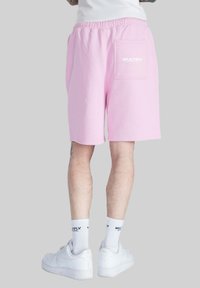 Pantalones cortos de algodón rosa con cintura elástica y un bolsillo trasero que presenta el texto "MULTIPLY". Usados con zapatillas blancas y calcetas.