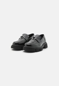 Mocasini din piele neagră, cu detaliu de cataramă. Acestea au o talpă groasă, texturată din cauciuc negru și un design cu vârf rotunjit.
