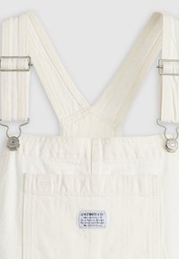 Salopette en jean blanche avec bretelles réglables et fermoirs métalliques, dotée d'une poche plaquée à l'avant avec une étiquette Levi Strauss & Co.