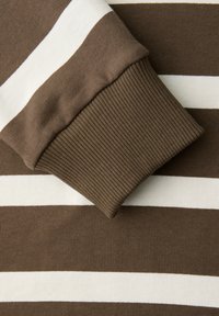 Nahaufnahme eines langärmeligen Hemdes mit braun-weißen horizontalen Streifen und gerippten Bündchen.