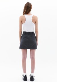 Grijze wol mini rok met een aangesloten taille, twee achterzakken en een gladde textuur. Draag het met een witte tanktop en zwarte schoenen.