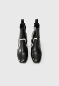 Bottines en cuir noir à bout carré, avec des coutures blanches sur les côtés et une fermeture éclair pour un enfilage facile.