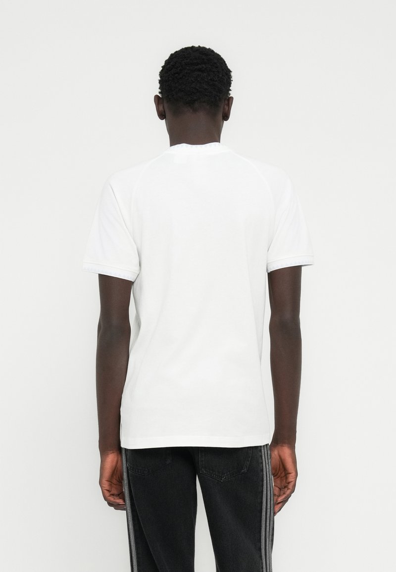 Maglietta bianca in cotone con maniche corte, scollo tondo e design semplice. Abbinata a jeans neri con strisce verticali.