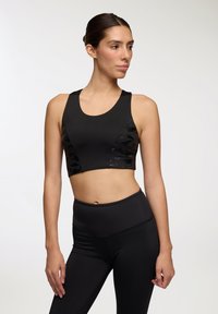 Top sportivo nero con tessuto liscio e accenti a motivo camouflage. Presenta un collo a barchetta ed è abbinato a leggings neri a vita alta.