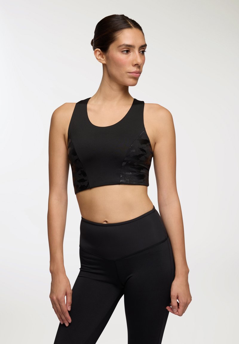 Top sportivo nero con tessuto liscio e accenti a motivo camouflage. Presenta un collo a barchetta ed è abbinato a leggings neri a vita alta.