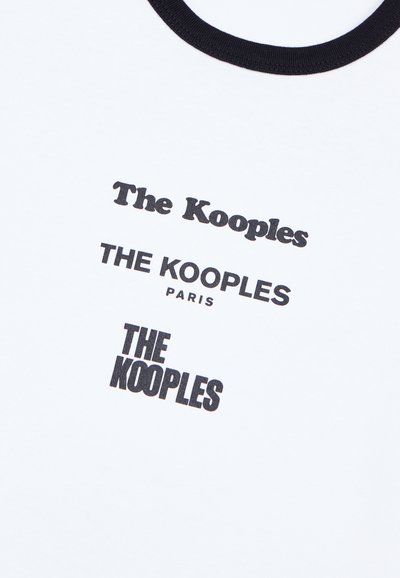 Weißes Baumwoll-T-Shirt mit rundem schwarzen Halsausschnitt, das wiederholt fettgedruckten schwarzen Text zeigt: "The Kooples" und "PARIS" in unterschiedlichen Größen.