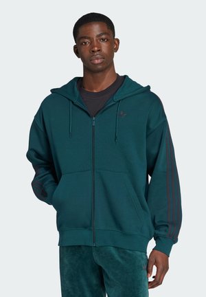 Felpa zip-up color teal in morbido tessuto con cappuccio, tasche anteriori e tre strisce scure lungo le maniche. Logo minimale sul petto.