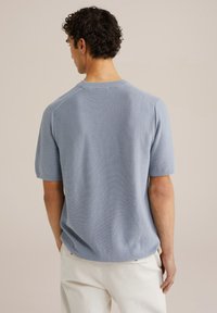 Short-sleeve knit top in light blue. Features a round neckline and soft texture. Back view shows raglan sleeves and a relaxed fit.