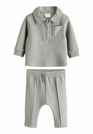 Ținută pentru bebeluși din două piese, de culoare gri, cu un top cu guler și fermoar, prevăzut cu un buzunar pe piept, și pantaloni asortați cu talie elastică, amândouă dintr-un material moale.