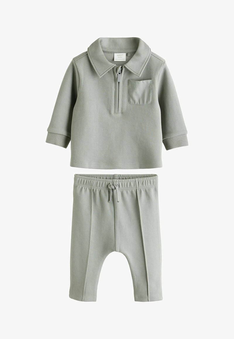 Ensemble pour bébé en deux pièces de couleur grise, comprenant un haut à col avec zipper et poche sur la poitrine, ainsi que des pantalons à taille élastique assortis, le tout en tissu doux.