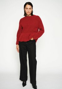 Maglione a maglia rosso con texture e design peplum, abbinato a pantaloni neri a gamba larga. Completato con tacchi neri a punta.