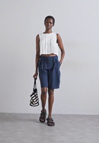 Biały, plisowany top crop, granatowe szorty w paski, czarne sandały i torebka w czarno-białym wzorze. Gładki materiał, luźny fason i casualowy design.