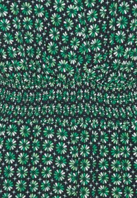 Tissu noir présentant un motif de fleurs vertes et blanches avec une taille smockée. Le design est uniforme et dense dans l'ensemble.