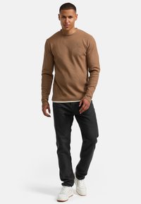 Hellbraunes, geripptes Langarmshirt kombiniert mit dunklen Jeans und weißen Sneakers. Das Shirt hat einen Rundhalsausschnitt und enganliegende Ärmel.