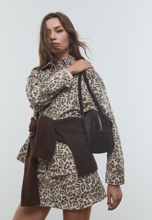 Giubbotto di jeans con stampa leopardata e gonna, abbinati a una borsa in velluto a coste marrone. Modella con una cintura in maglione marrone attorno alla vita, con dettagli testurizzati ben visibili.