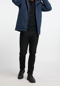 Veste matelassée bleu marine avec fermeture éclair, portée sur un t-shirt noir, associée à un jean noir et des baskets noires. Textures unies.
