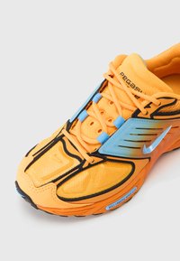 Sapatilha desportiva com um vibrante upper em malha laranja, detalhes em preto, componentes em azul e um design texturizado. Destaca-se pela sua construção leve.