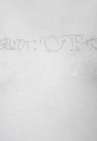 Bílé bavlněné tričko s mírně vystouplým, tónovaným tiskem názvu značky "Marc O'Polo" přes hruď. Lehká, hladká textura.