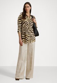 Beige og brun zebra-stripet skjorte med knapper, parret med kremfargede bukser med vid ben. Tilbehør med en svart skulderveske. Jevn tekstur i stoffet.