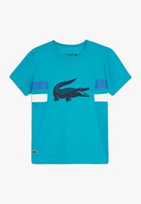 Turkusowy bawełniany t-shirt z czarną grafiką krokodyla oraz niebieskimi i białymi poziomymi paskami na rękawach. Dekolt okrągły.