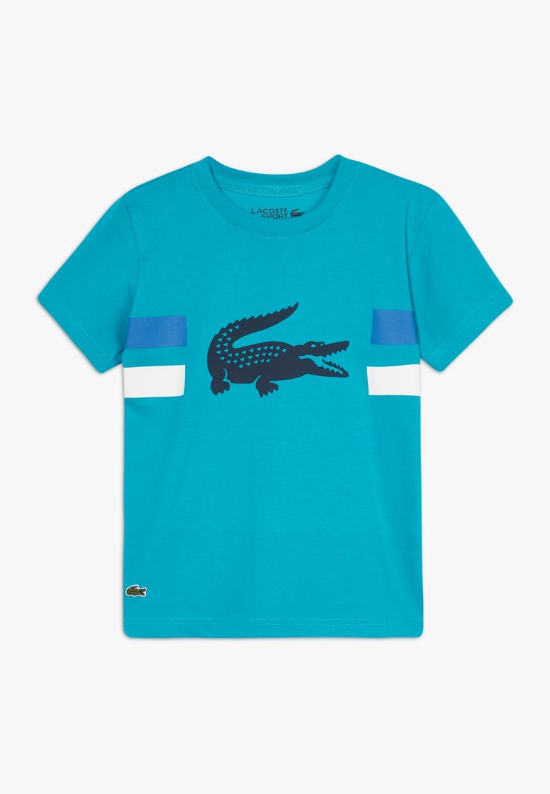 Turkusowy bawełniany t-shirt z czarną grafiką krokodyla oraz niebieskimi i białymi poziomymi paskami na rękawach. Dekolt okrągły.