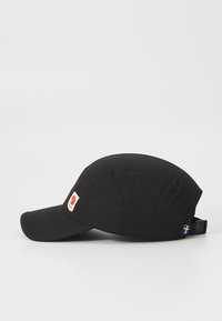 Crna kapa s zakrivljenim vizirjem, tkanina teksture, bočni logo patch i podesivi remen s malim naglaskom na švedsku zastavu.