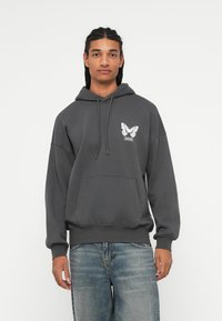 Hoodie grigio in cotone con tasca frontale, cappuccio con cordino e grafica di una farfalla sul lato sinistro del petto. Vestibilità comoda e texture morbida.