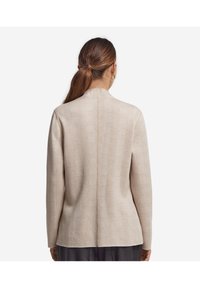 Beige strukturerad cardigan med en lätt rutmönster, långa ärmar och en avslappnad passform. Har en rundad halsringning och detalj på bakseam.