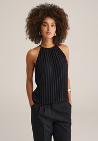 Čierny plisovaný halter top s textúrovaným dizajnom, so zaobleným výstrihom a voľným strihom, skombinovaný s ušitými čiernymi nohavicami.