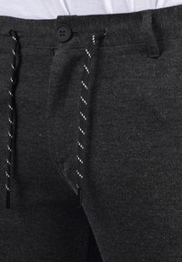 Pantalones de color gris oscuro con una textura suave, cierre frontal con botón y cordón de contraste en blanco y negro con puntas de plástico.