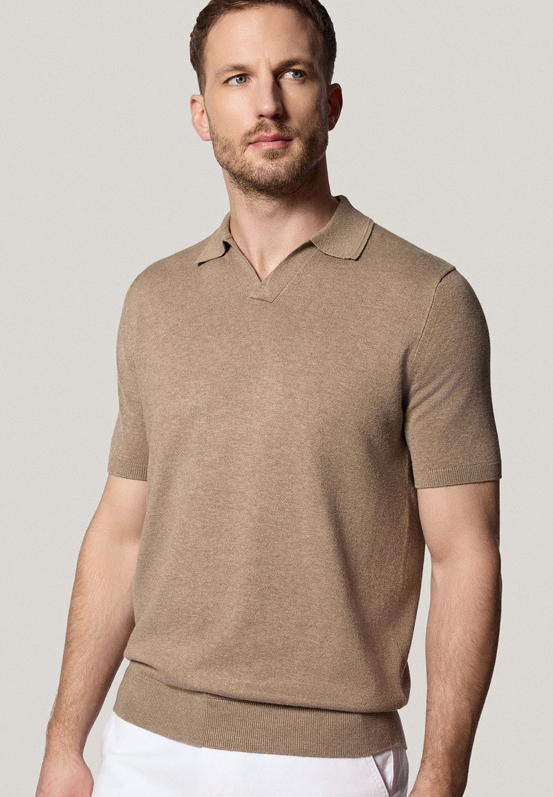 Beżowa koszulka polo z krótkim rękawem, z dekoltem w serek i ściągaczem na dole. Miękka faktura i czysty design. Noszona z białymi spodniami.