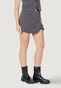 Completo grigio a righe sottili composto da gilet e gonna dal taglio aderente con due tasche laterali, abbinato a stivaletti neri lucidi con suole spesse.