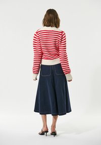 Maglione lavorato a maglia a righe rosse e bianche con collo alto e polsini a costine, abbinato a una gonna A-line blu scuro e sandali neri con tacco.